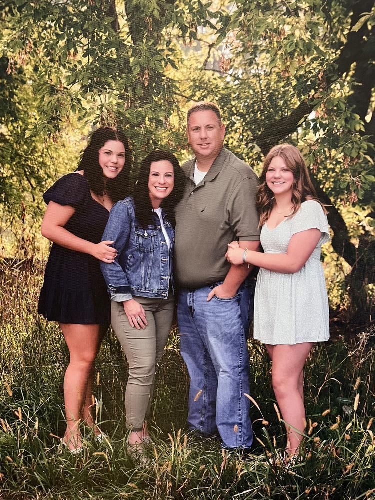 Four people posing together outdoors in front of trees, smiling at the camera.