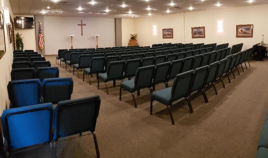 Empty church hall with rows of green chairs facing a wall cross and framed pictures