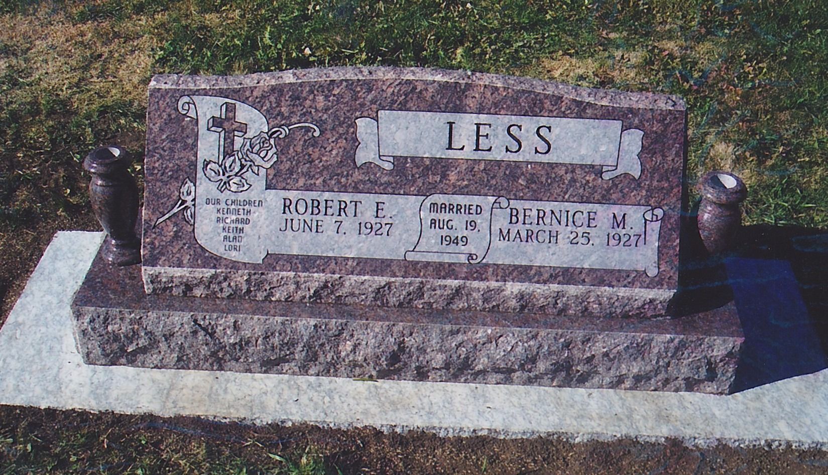 Gravestone with the name “LESS” on a pink granite headstone in a cemetery setting