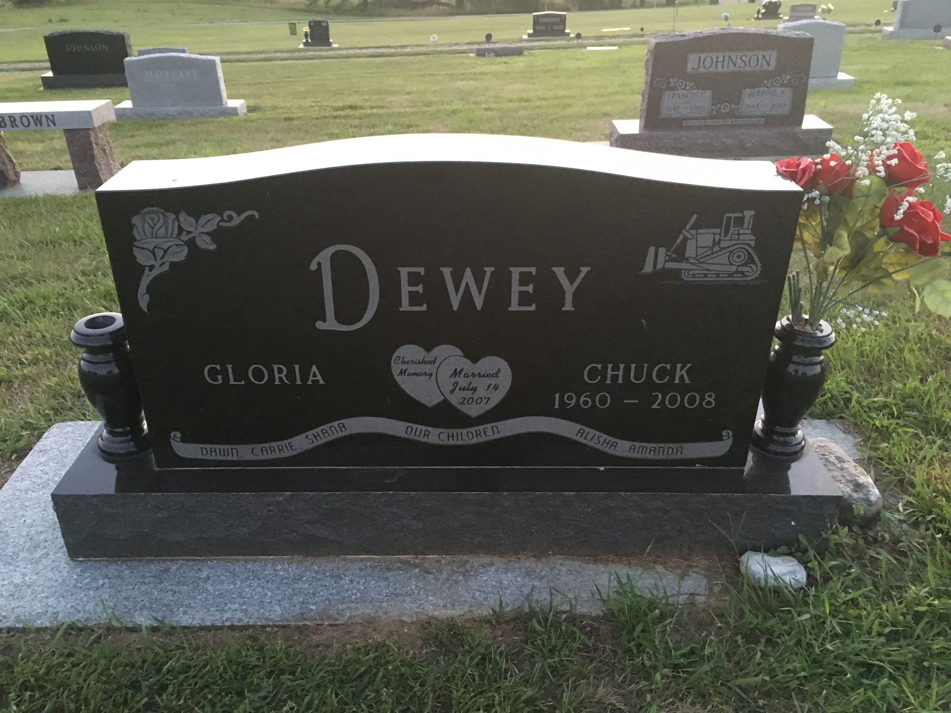 Black headstone in a cemetery engraved “Dewey,” with flowers on the right.