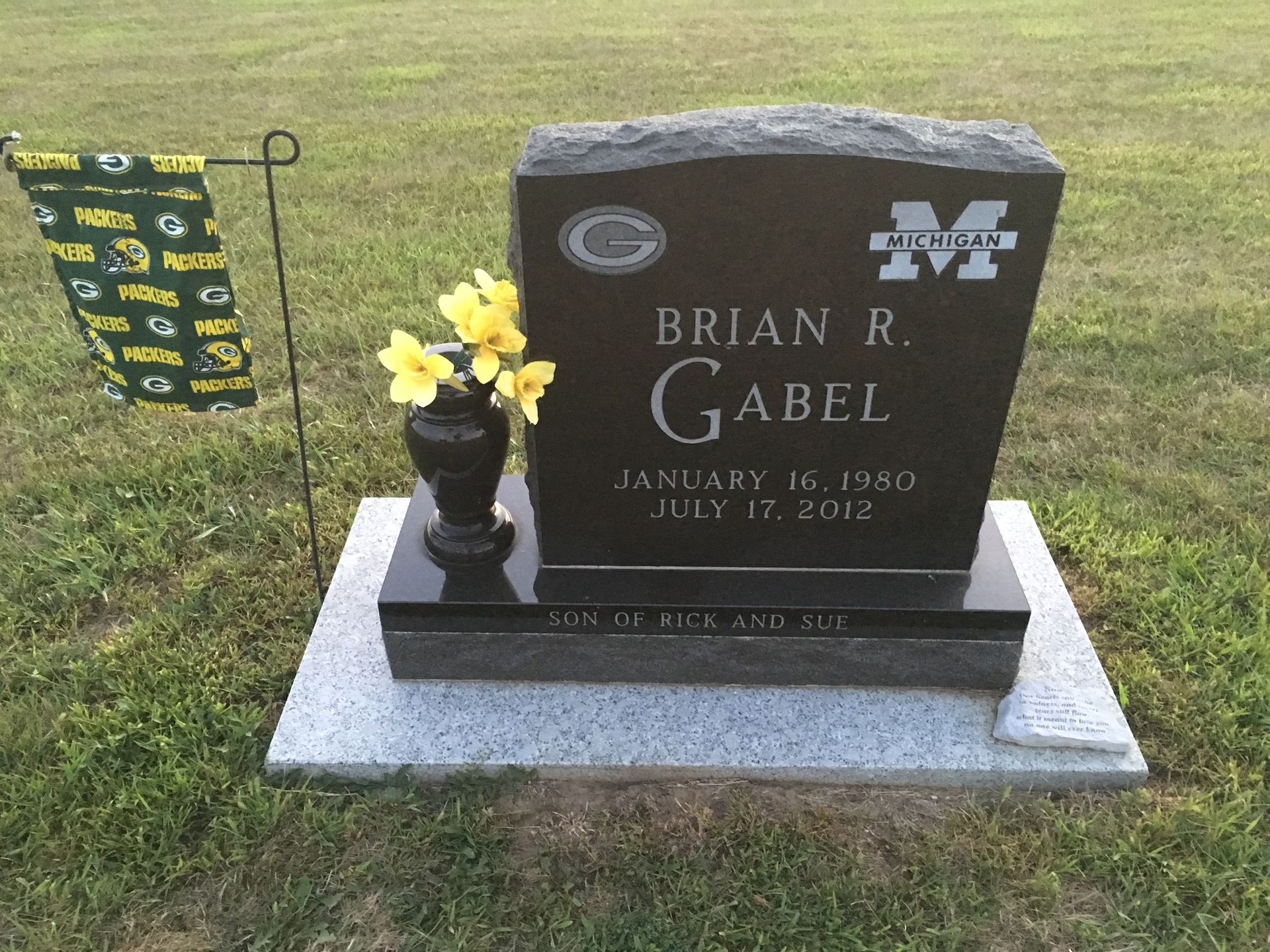 Gravestone for Brian R. Gabel with yellow flowers and a small flag in a cemetery.