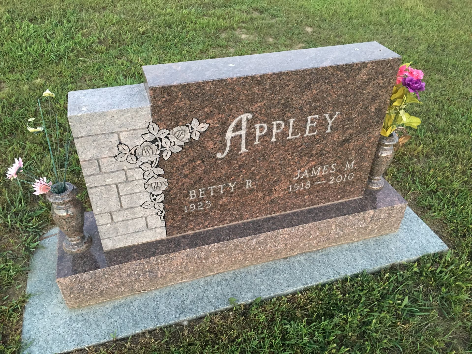 Appley gravestone with flowers on a grassy lawn, featuring a split light and dark stone memorial.