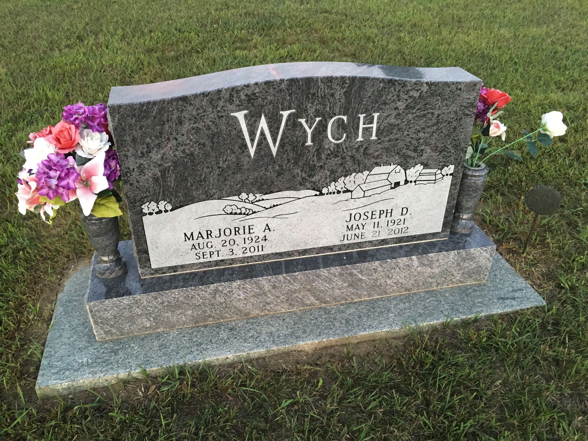 Wych gravestone on grass with flowers on both sides and engraved names on a gray monument