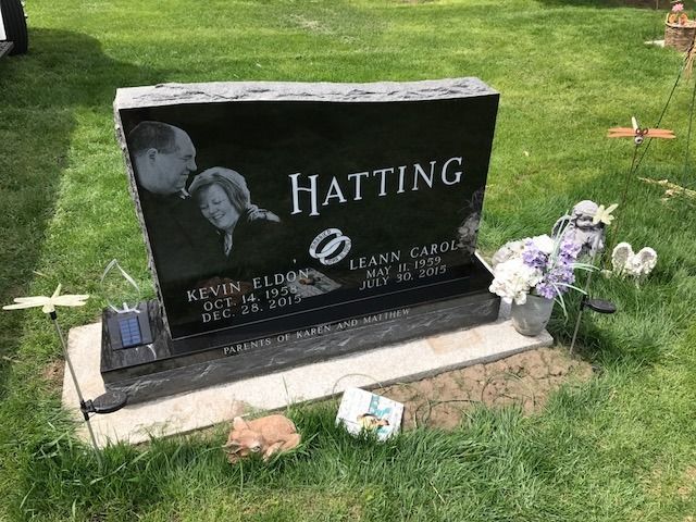 Black granite memorial headstone with flowers on a grassy lawn