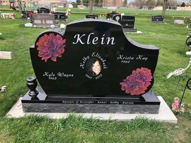 Black gravestone with “Klein” and red flowers in a cemetery