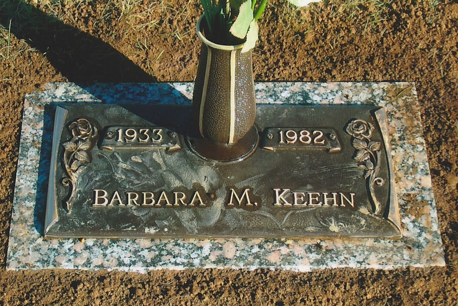 Gravestone for Barbara M. Keenn with engraved dates 1933–1982 and flowers above on grass
