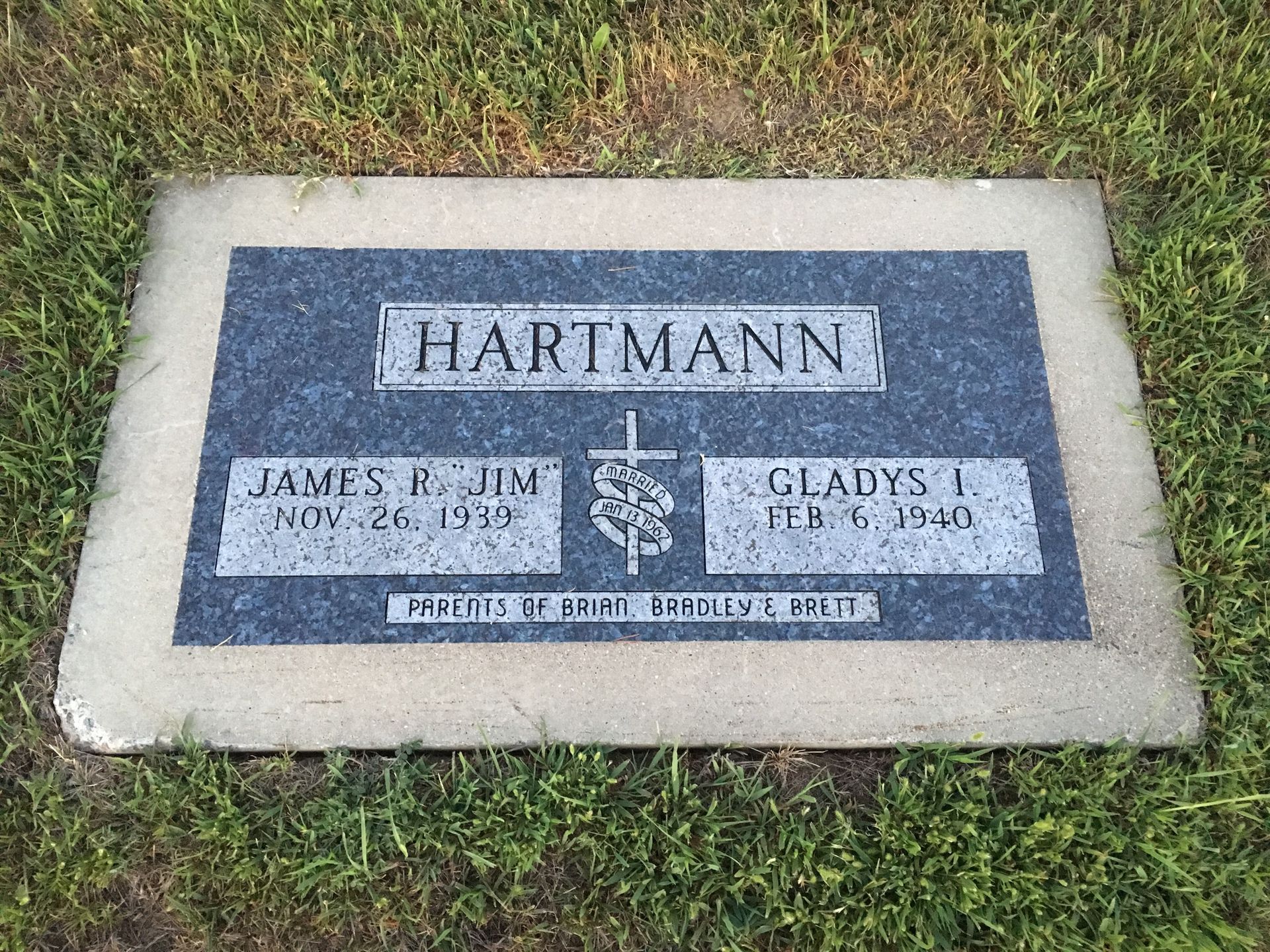 Gray cemetery headstone with engraved names Hartmann, James E. Rush, and Gladys F. on grass
