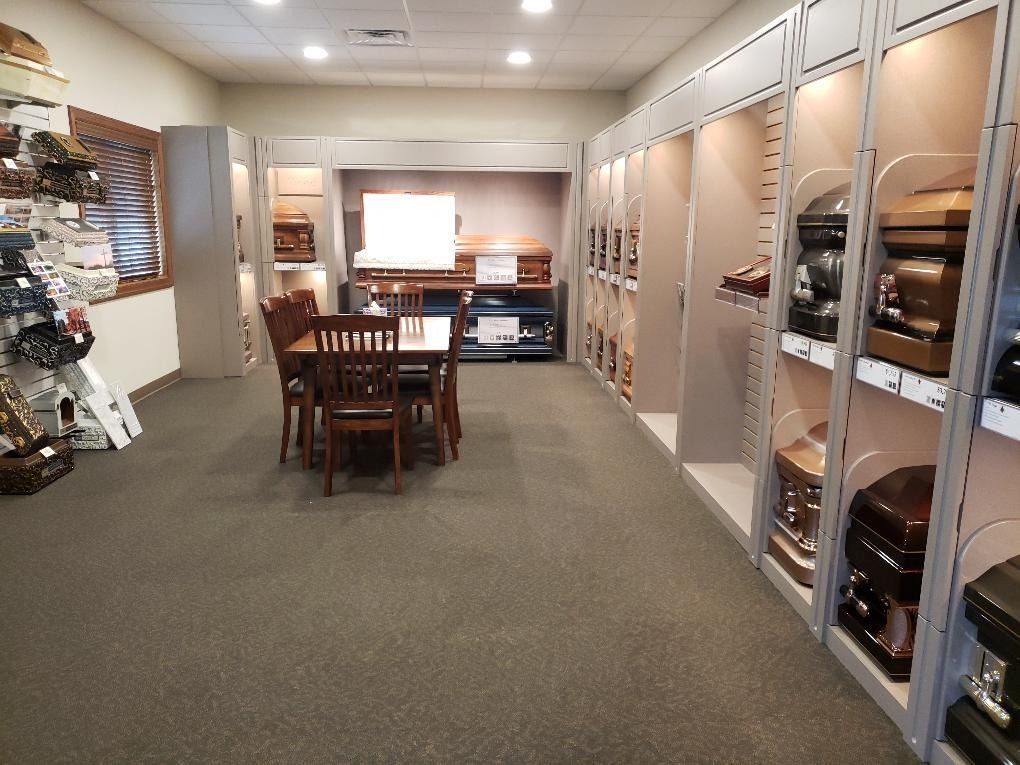 Carpeted showroom with wooden furniture displays, shelving, and a dining table under bright ceiling lights