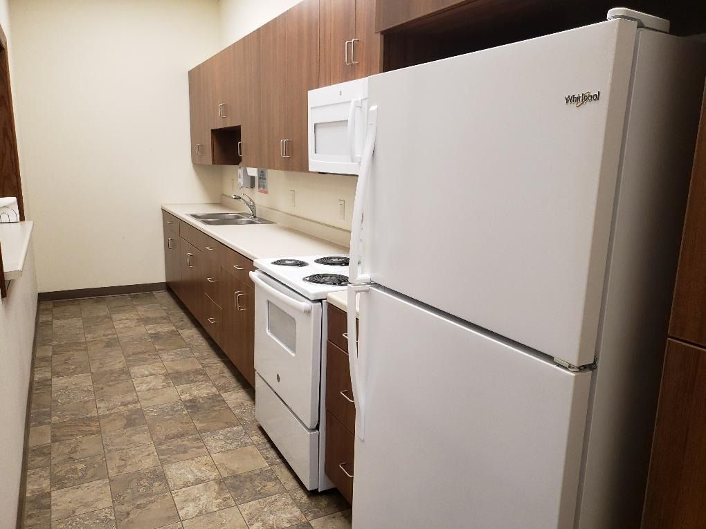 Small apartment kitchen with white appliances, brown cabinets, and patterned linoleum floor.