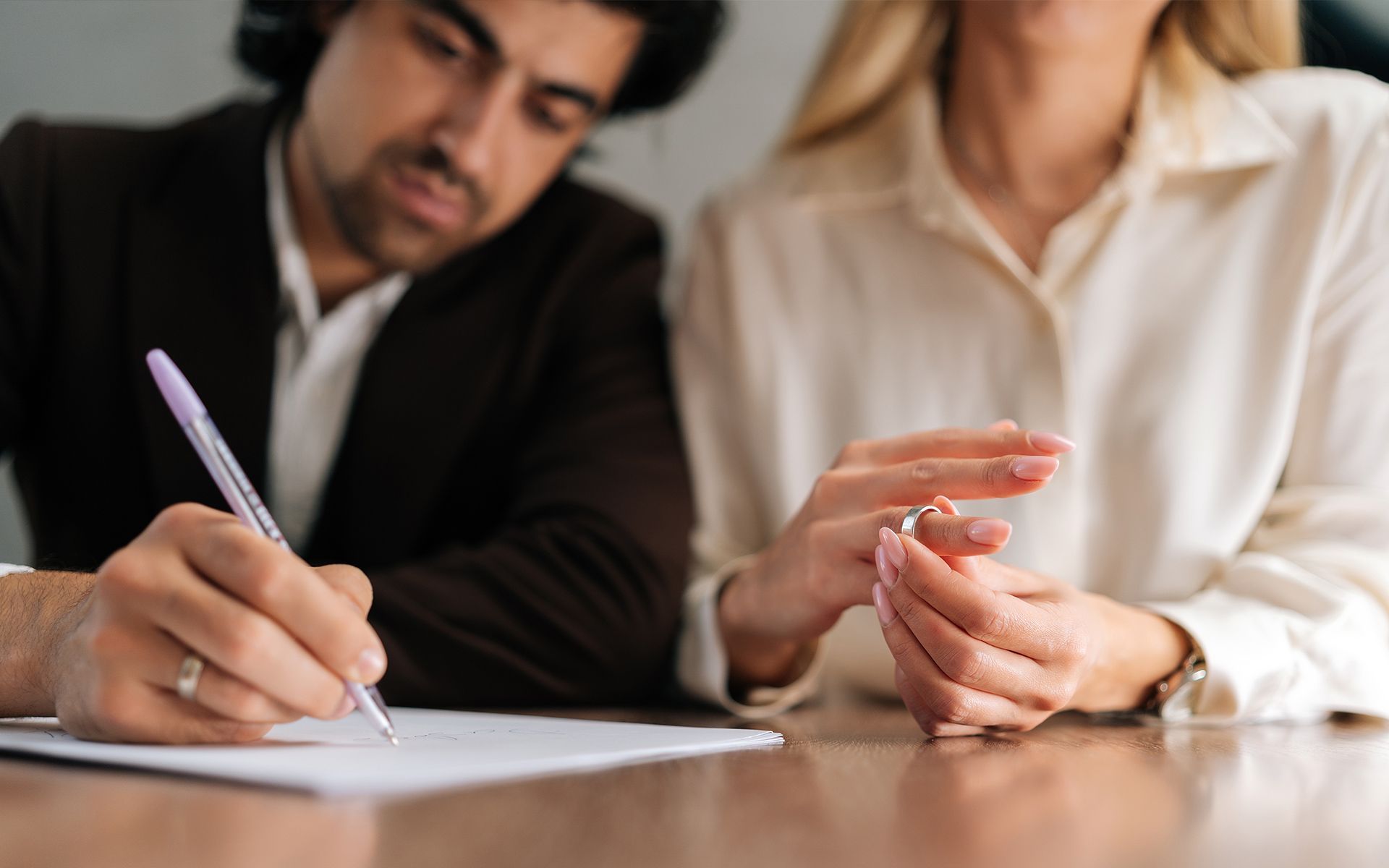 Man signing a document, while woman removes wedding ring.