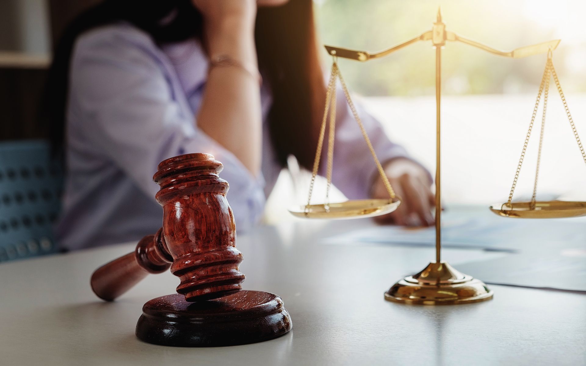 Wooden gavel, balance scales, and person in a legal setting, possibly a lawyer or judge.