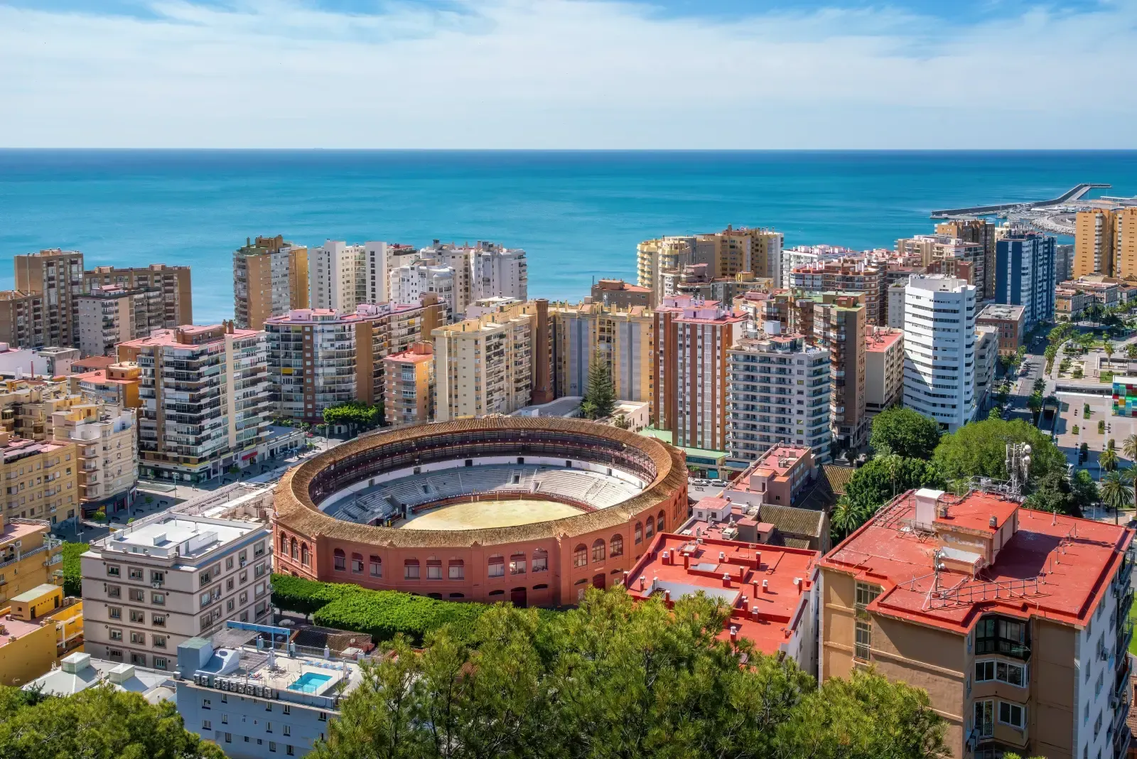 An aerial view of the Plaza de Toros de la Malagueta bullring in Malaga, Spain, surrounded by city buildings and the sea.