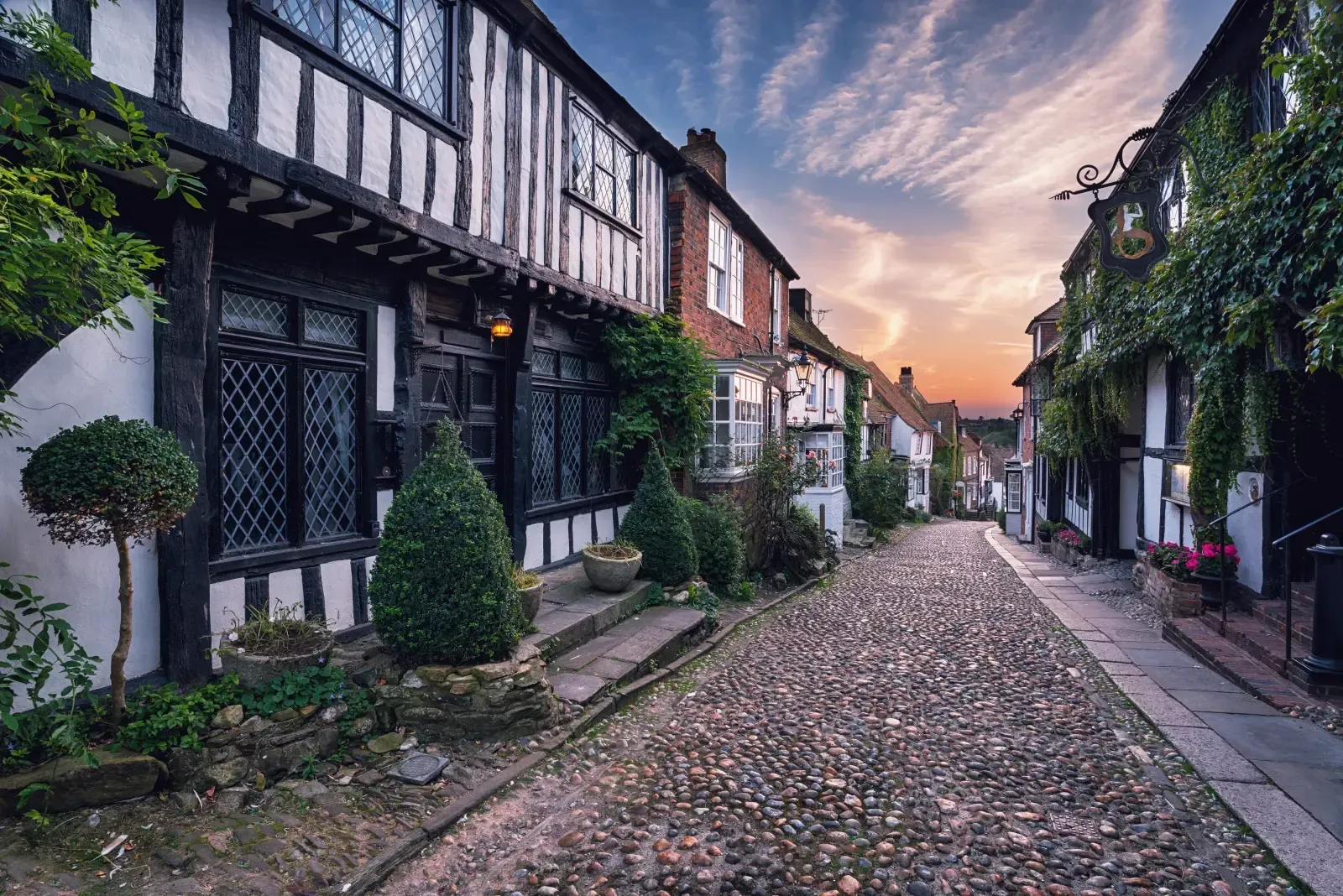 A picturesque, cobblestone street lined with historic timber-framed houses at sunset.
