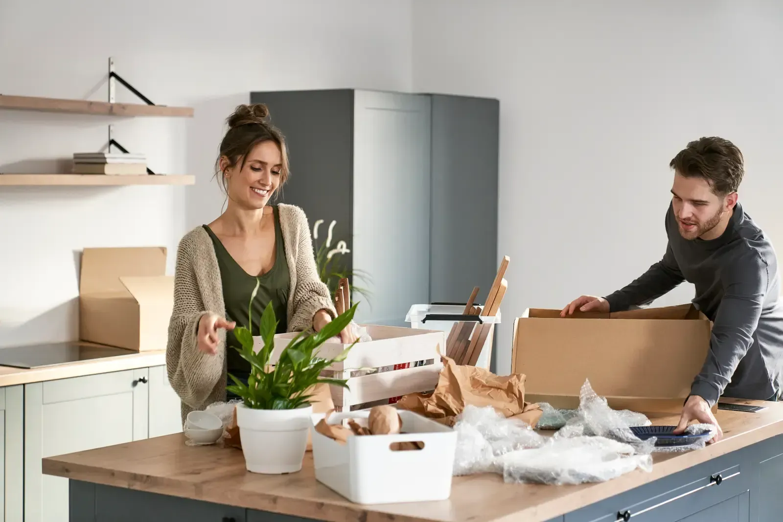 Two people packing boxes at a kitchen table with plants and shipping materials