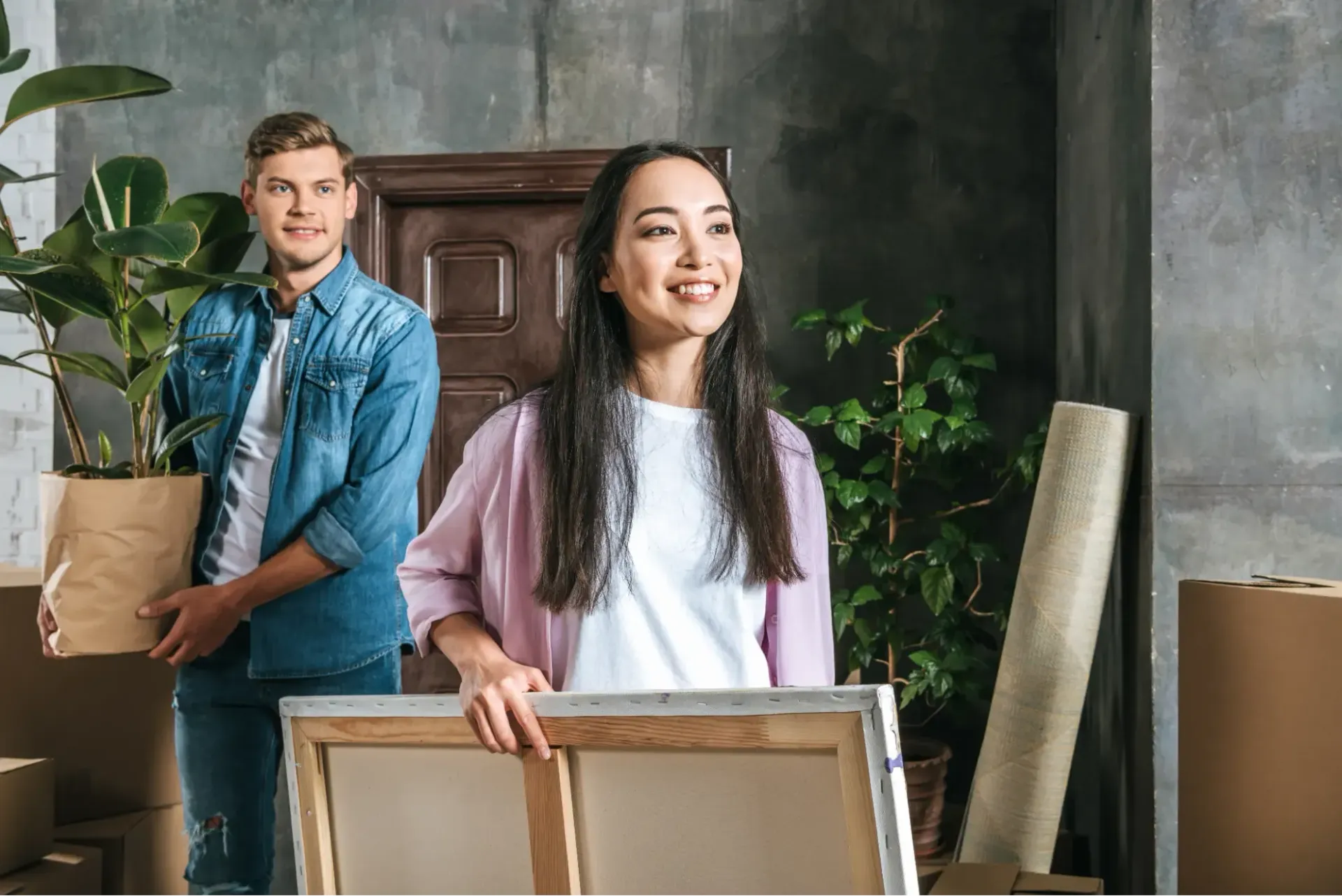 A man and a woman are moving into a new house . the woman is holding a painting.