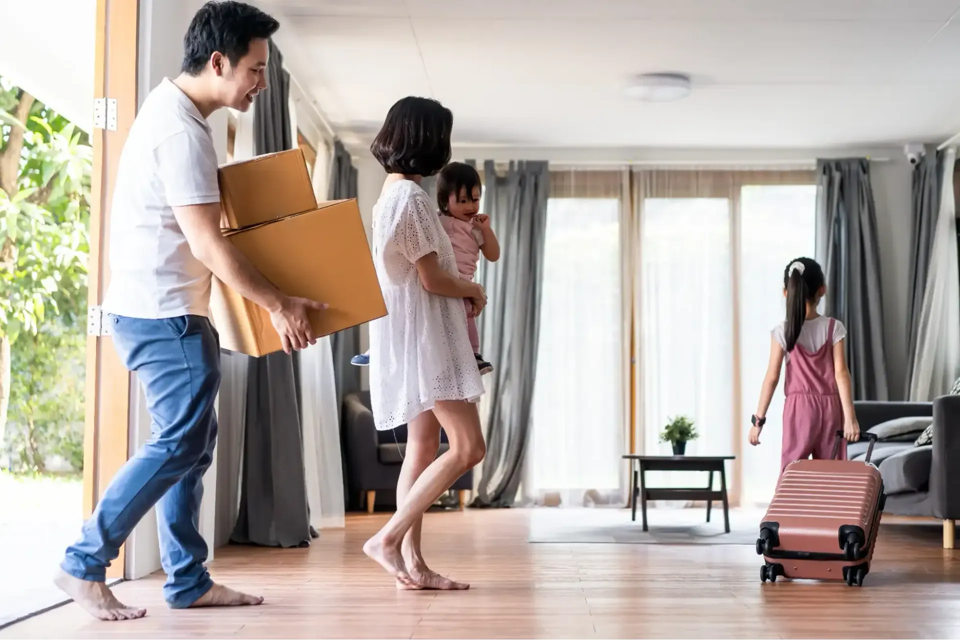 A family is moving into a new home and carrying boxes and a suitcase.