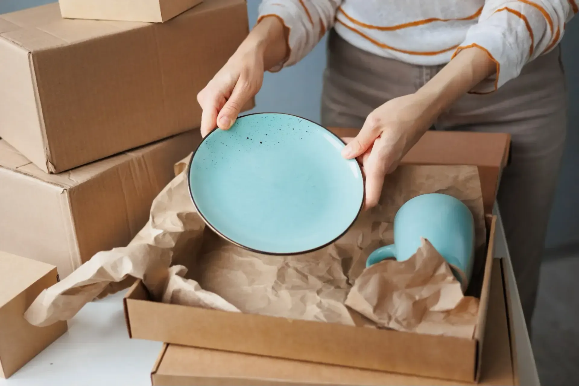 Hands packing up dishes into moving box