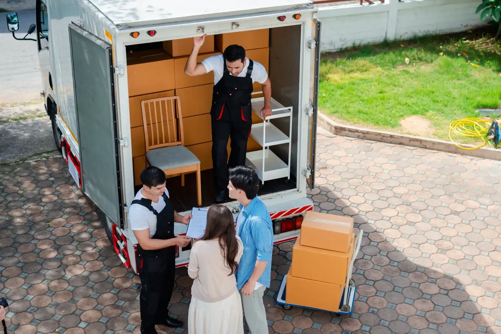 People unloading cardboard boxes from a delivery truck beside a sidewalk