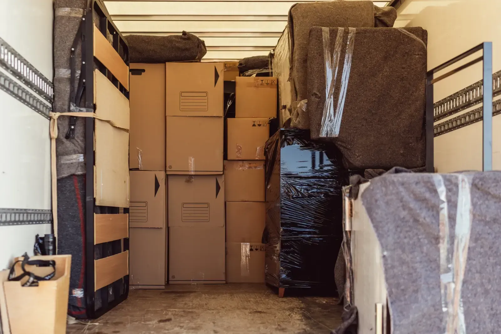 Packed moving truck with stacked cardboard boxes and wrapped furniture inside