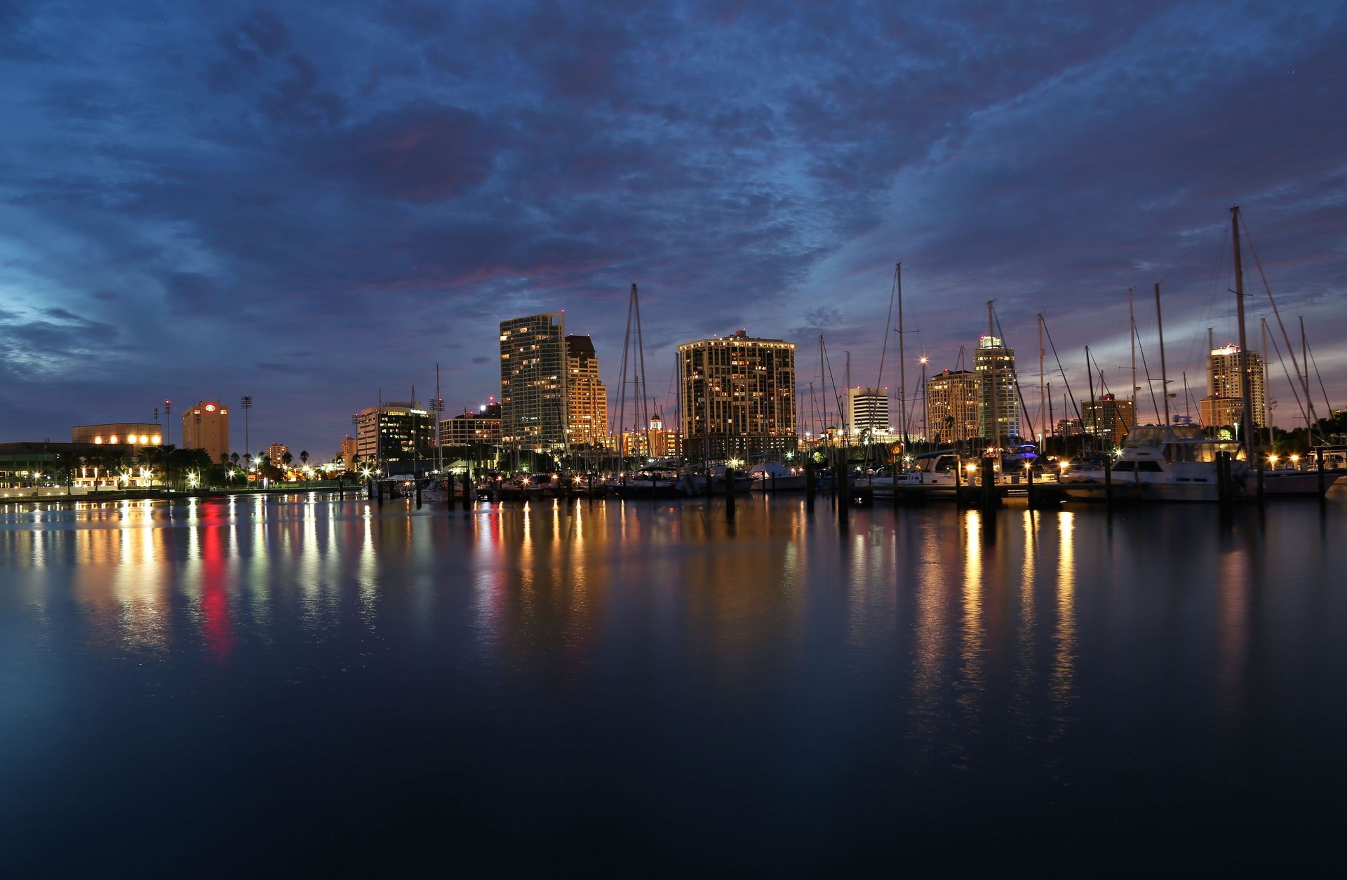 City skyline at dusk with lit buildings reflecting on calm water under a deep blue sky
