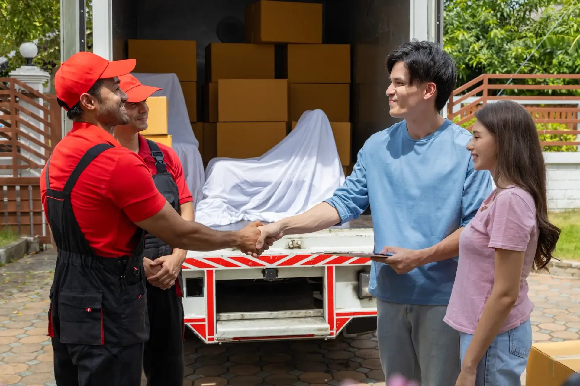Two movers shake hands with a couple in front of a moving truck filled with boxes.
