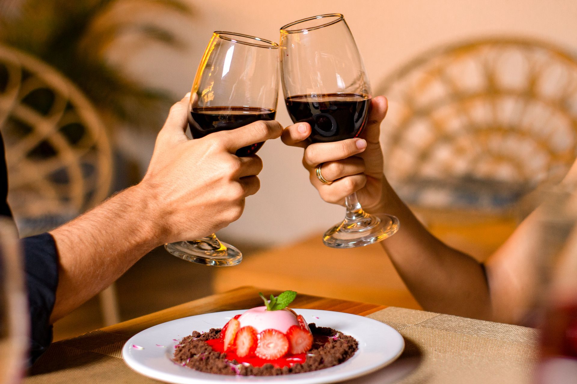 Dos personas brindan con copas de vino tinto mientras comparten un postre coronado con fresas.