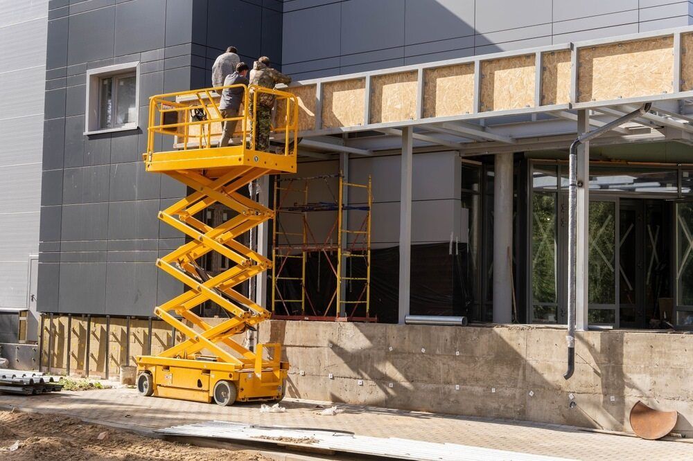 A Man is Standing on a Scissor Lift in Front of a Building — FNQ Hot Water In Mareeba, QLD