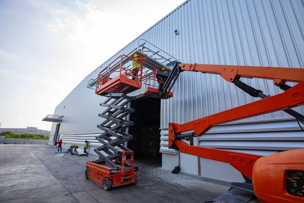 A Man is Standing on a Scissor Lift in Front of a Building — FNQ Hot Water In Mareeba, QLD
