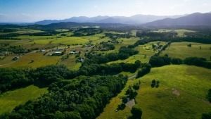 An Aerial View of a Lush Green Field With Trees and Mountains in the Background — FNQ Hot Water In Port Douglas, QLD