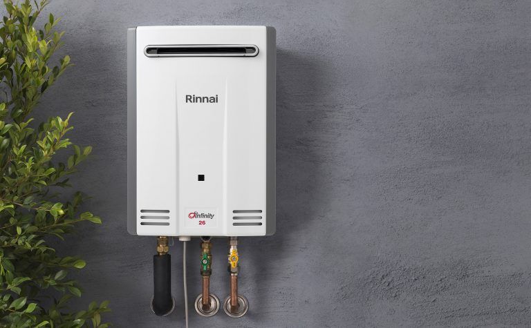A White Water Heater is Hanging on a Wall Next to a Tree — FNQ Hot Water In Mareeba, QLD