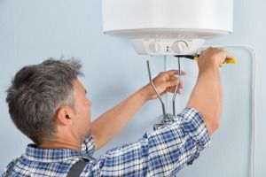 A Man Is Installing A Water Heater On A Wall — FNQ Hot Water In Cairns, QLD