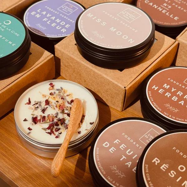 Bougies parfumées assorties dans des boîtes et des contenants ronds, disposées sur une table en bois, dont une bougie ouverte avec un coupe-mèche.