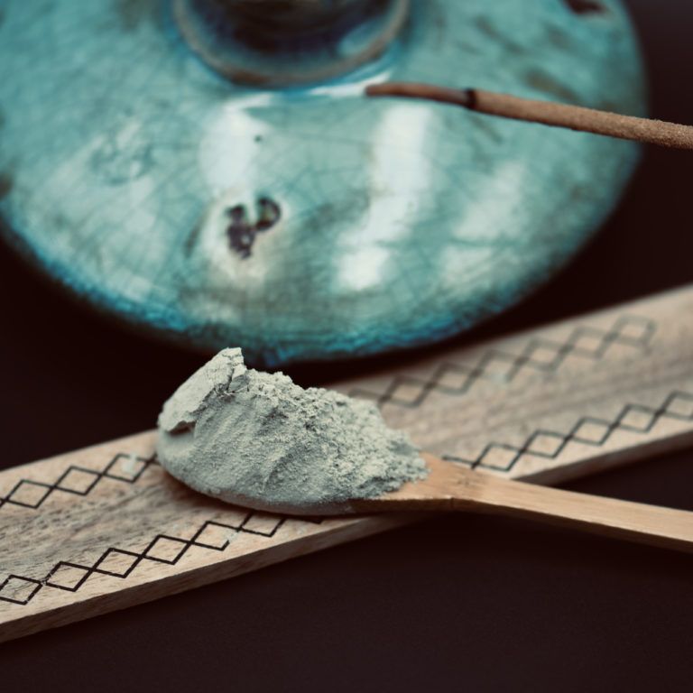Récipient cosmétique bleu contenant de la poudre de maquillage sur une spatule posée sur une bande de papier à motifs