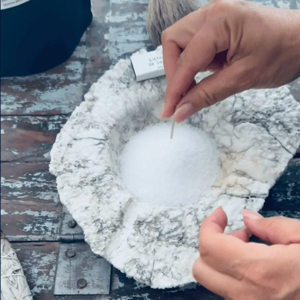 Personne utilisant un cure-dent dans un bol de cristaux blancs, peut-être du sel, dans une pierre sculptée.