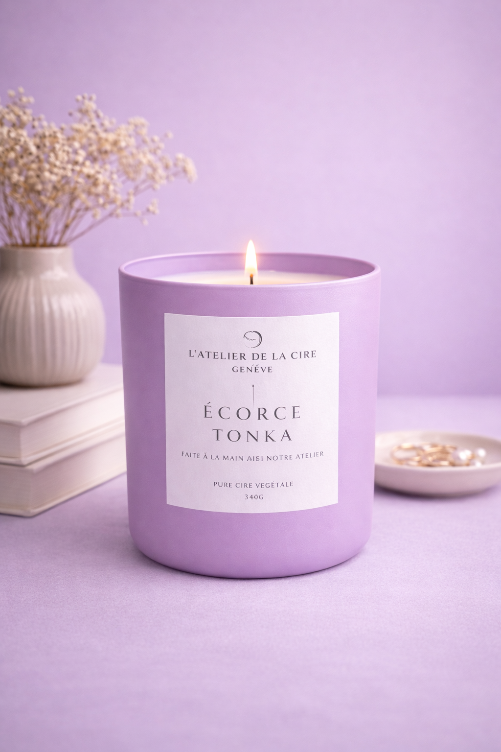 Bougie lavande allumée, étiquetée « Ecorce Tonka », posée sur une surface violette assortie, avec des fleurs séchées à proximité.