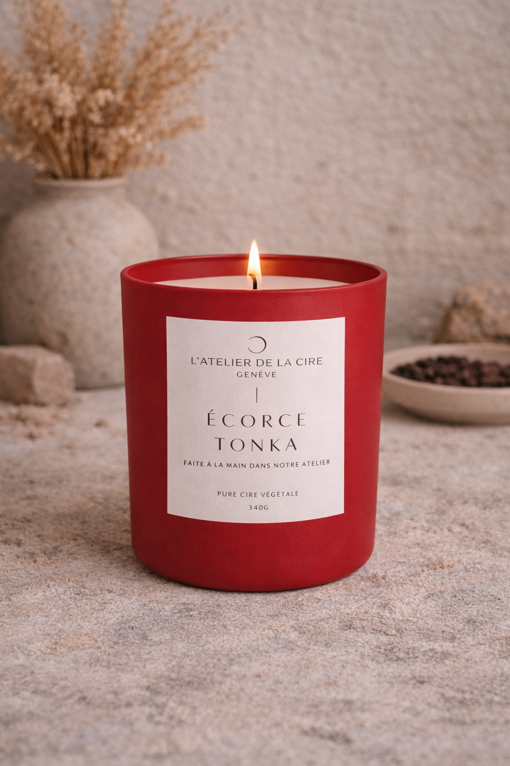 Bougie parfumée rouge brûlant sur une surface beige avec des fleurs séchées en arrière-plan