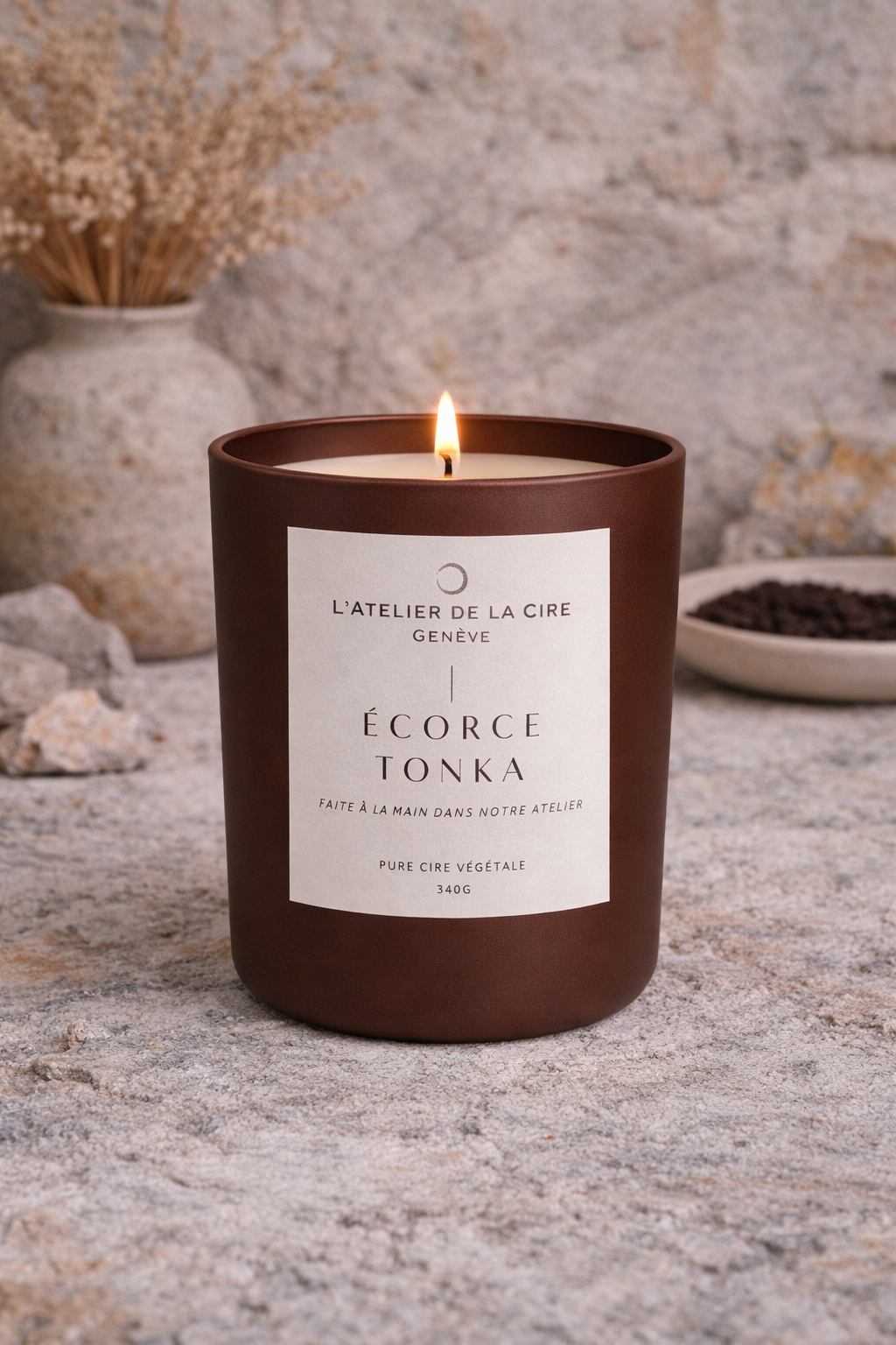 Bougie parfumée brune dans un pot en verre, avec une flamme allumée sur une surface en pierre, sur fond rustique.