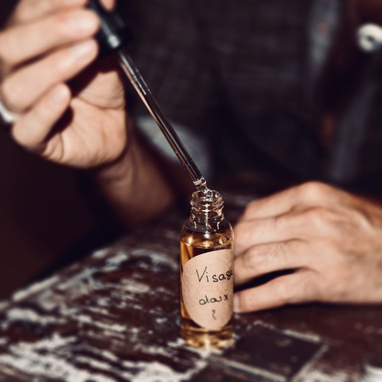 Une main utilise un compte-gouttes pour remplir une petite bouteille ambrée étiquetée « Visa » sur une table usée.