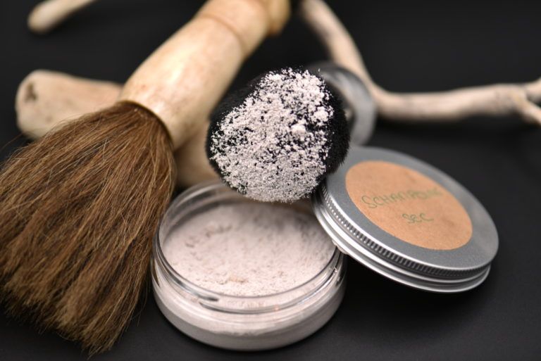 Pinceau de maquillage, poudrier et pots de poudre libre sur une surface sombre