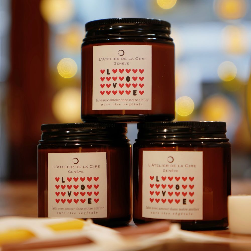 Trois bougies noires aux étiquettes en forme de cœur sur une table, sur un fond chaud légèrement flouté.