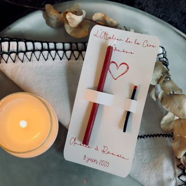 Carte blanche avec stylo rouge, petite bougie et fleurs séchées sur un tapis tissé.