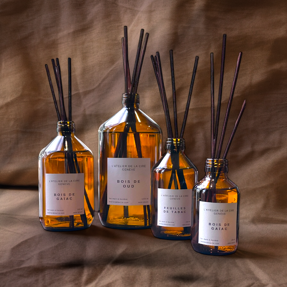 Quatre diffuseurs de roseaux en verre ambré avec des roseaux bruns sur un fond en tissu marron.