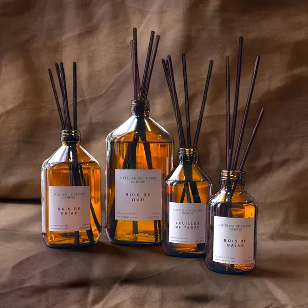 Quatre diffuseurs de parfum ambrés avec des bâtonnets noirs sur un fond de tissu marron.