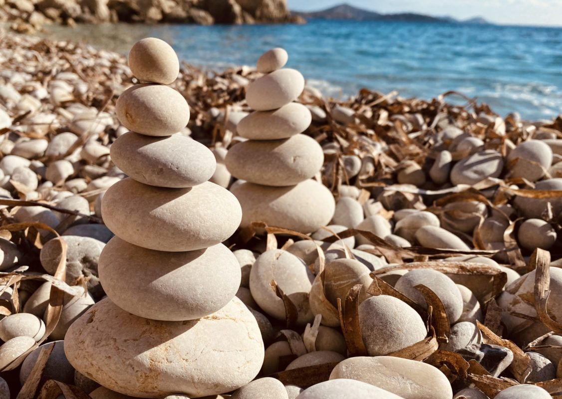 Two stacks of rounded stones on a beach with blue water and sky in the background.