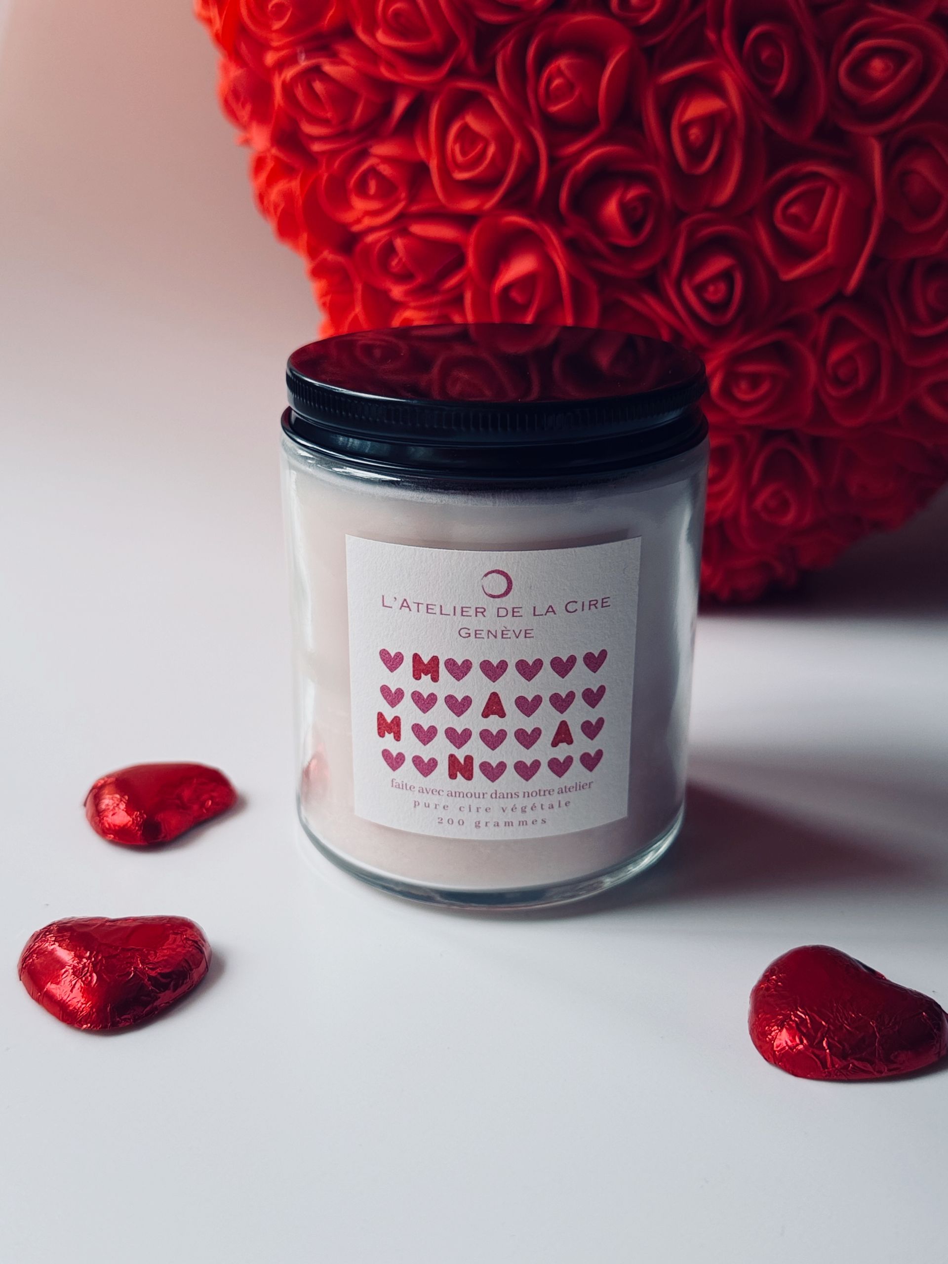 Bougie blanche dans un bocal en verre orné de cœurs rouges et d'un fond flou en forme de cœur de rose rouge.
