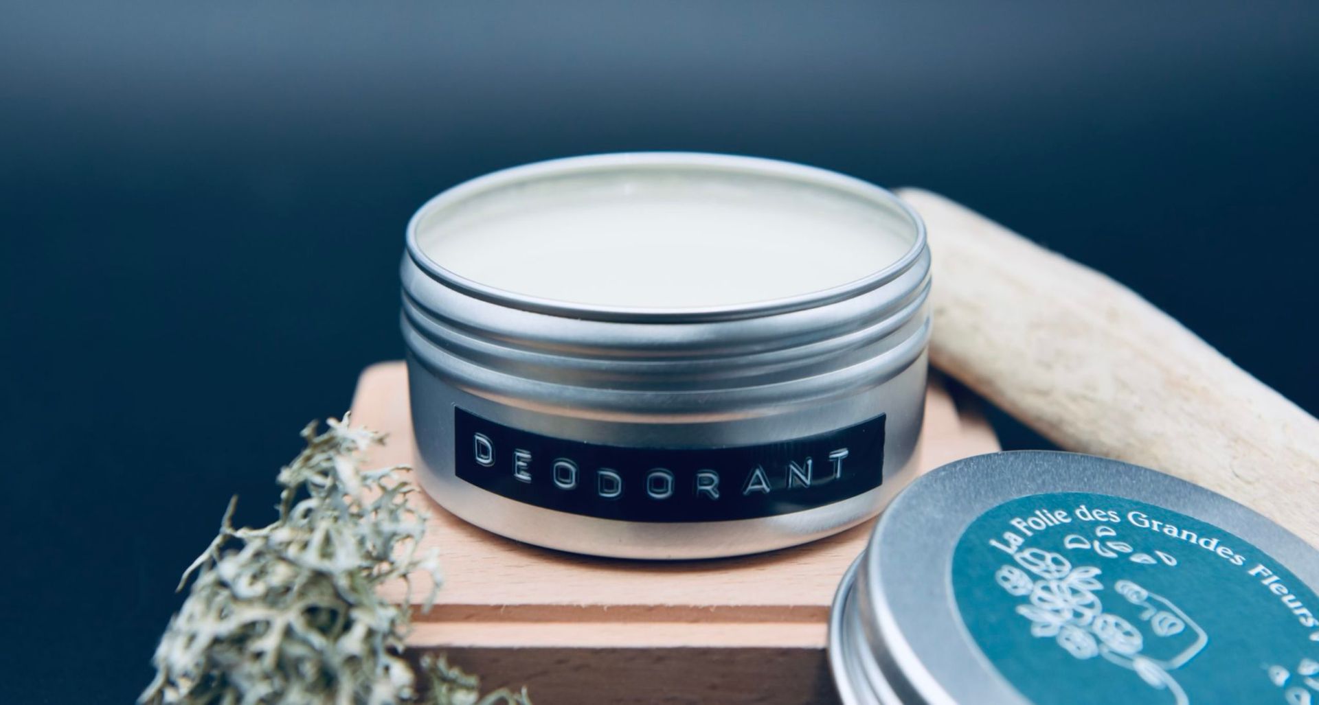 Deodorant jar with label on a wooden block. Gray metal container with white deodorant inside.
