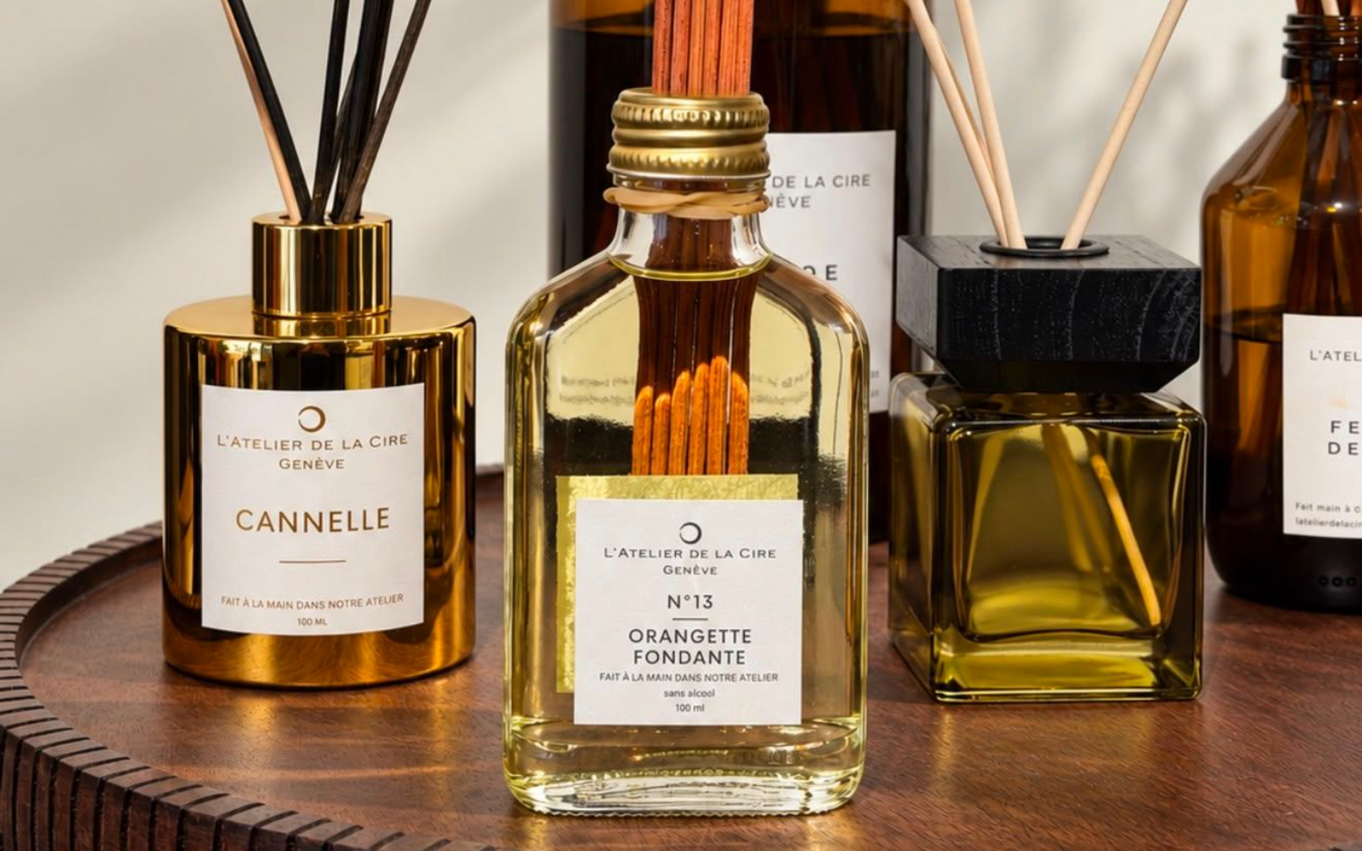 Quatre diffuseurs de parfum ambrés avec des bâtonnets noirs sur un fond de tissu marron.