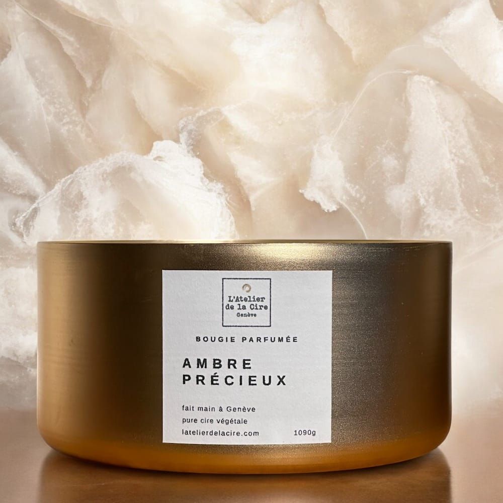Pot à bougie doré étiqueté « Ambre Précieux » sur fond de pierre beige