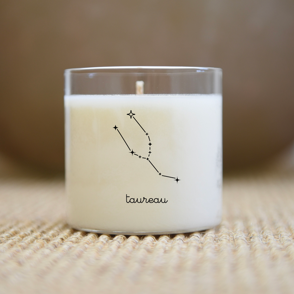 Bougie blanche dans un pot en verre transparent orné d'un motif de branche simple et du mot « taupeau ».