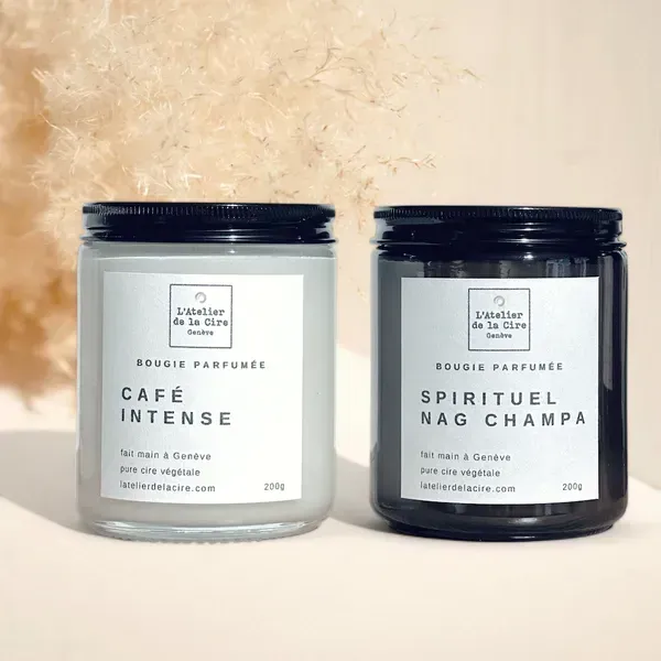 Deux pots à bougies parfumées, l'un blanc dépoli et l'autre gris foncé, étiquetés Café Intense et Spiritual Nag Champa.